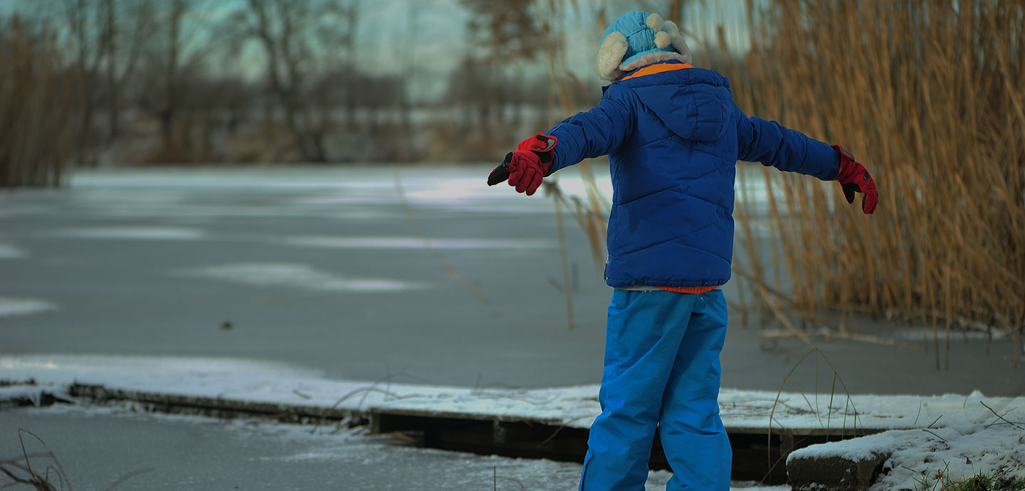 En dreng med udfoldede arme træder ud på en frossen sø