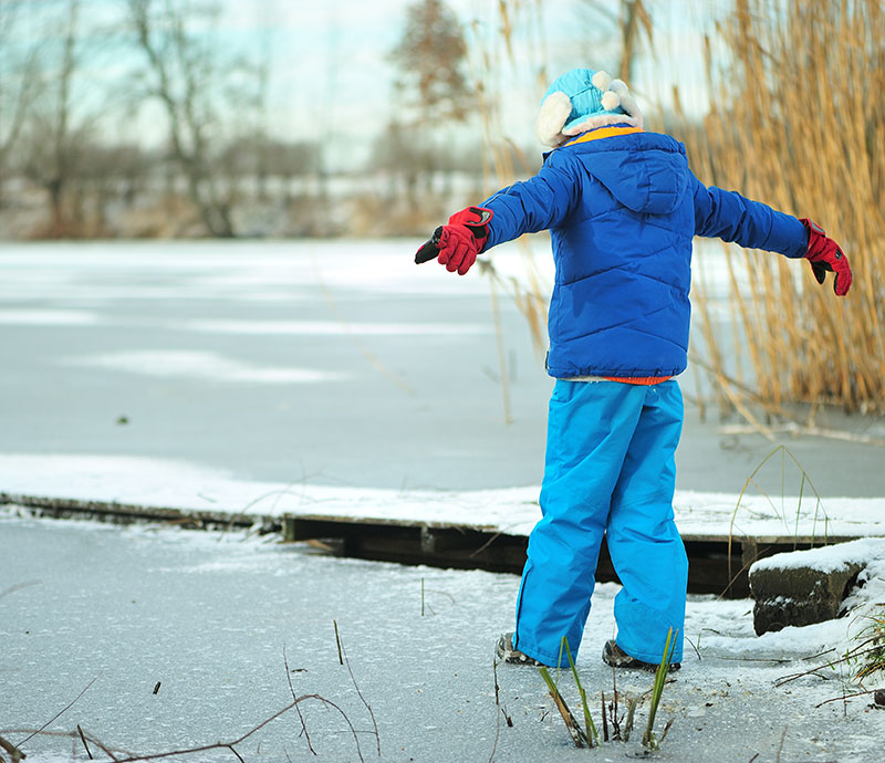 En dreng med udfoldede arme træder ud på en frossen sø