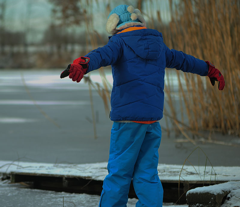 En dreng med udfoldede arme træder ud på en frossen sø