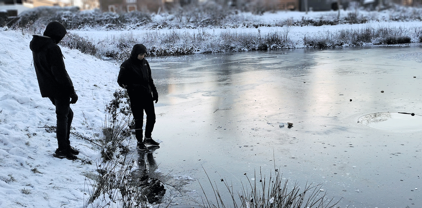 En person træder ud på en frossen sø, mens en anden kigger på fra bredden