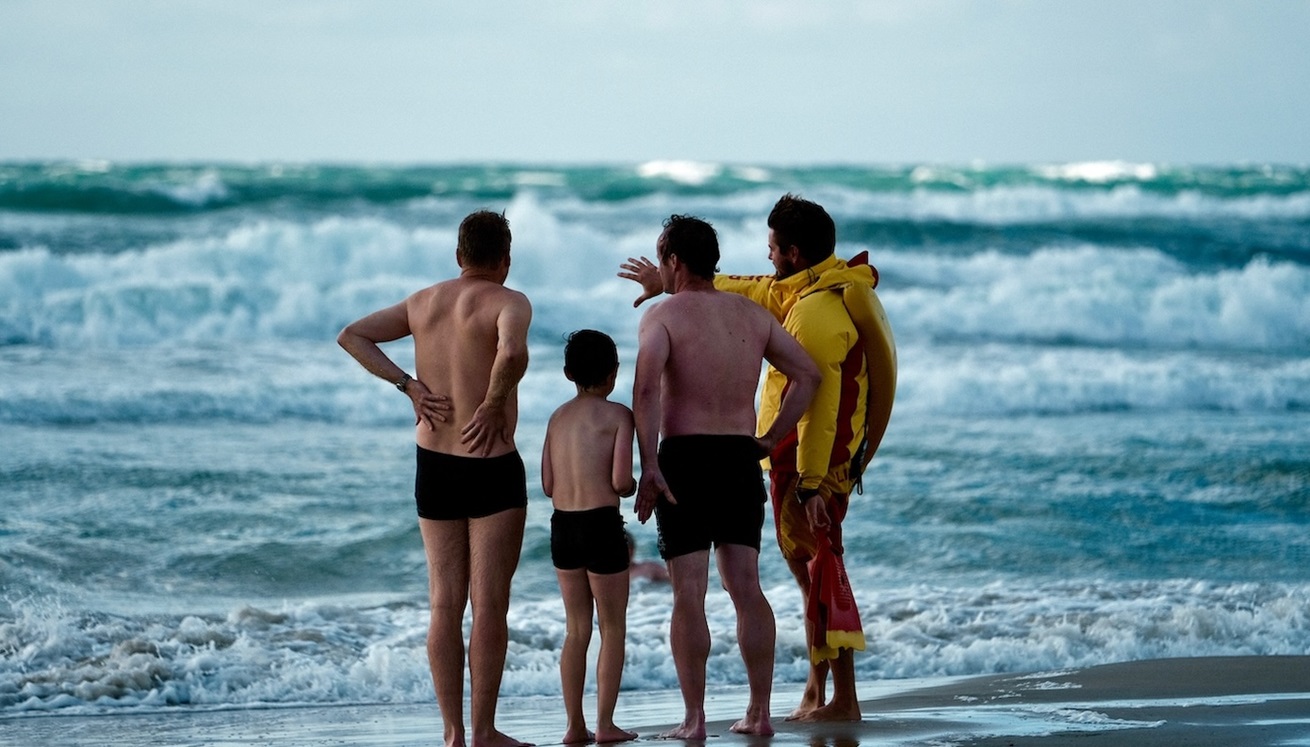 4 personer står på stranden og kigger på havet