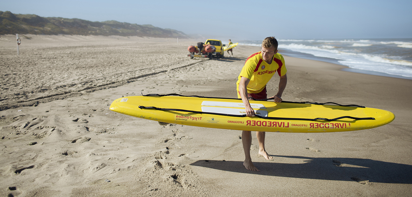 Livredder med surfbræt på stranden