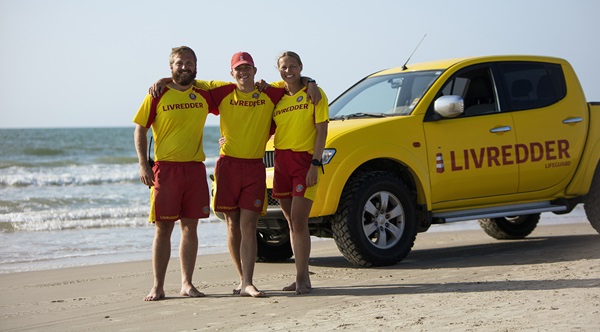 Tre livreddere foran en livredderbil på stranden