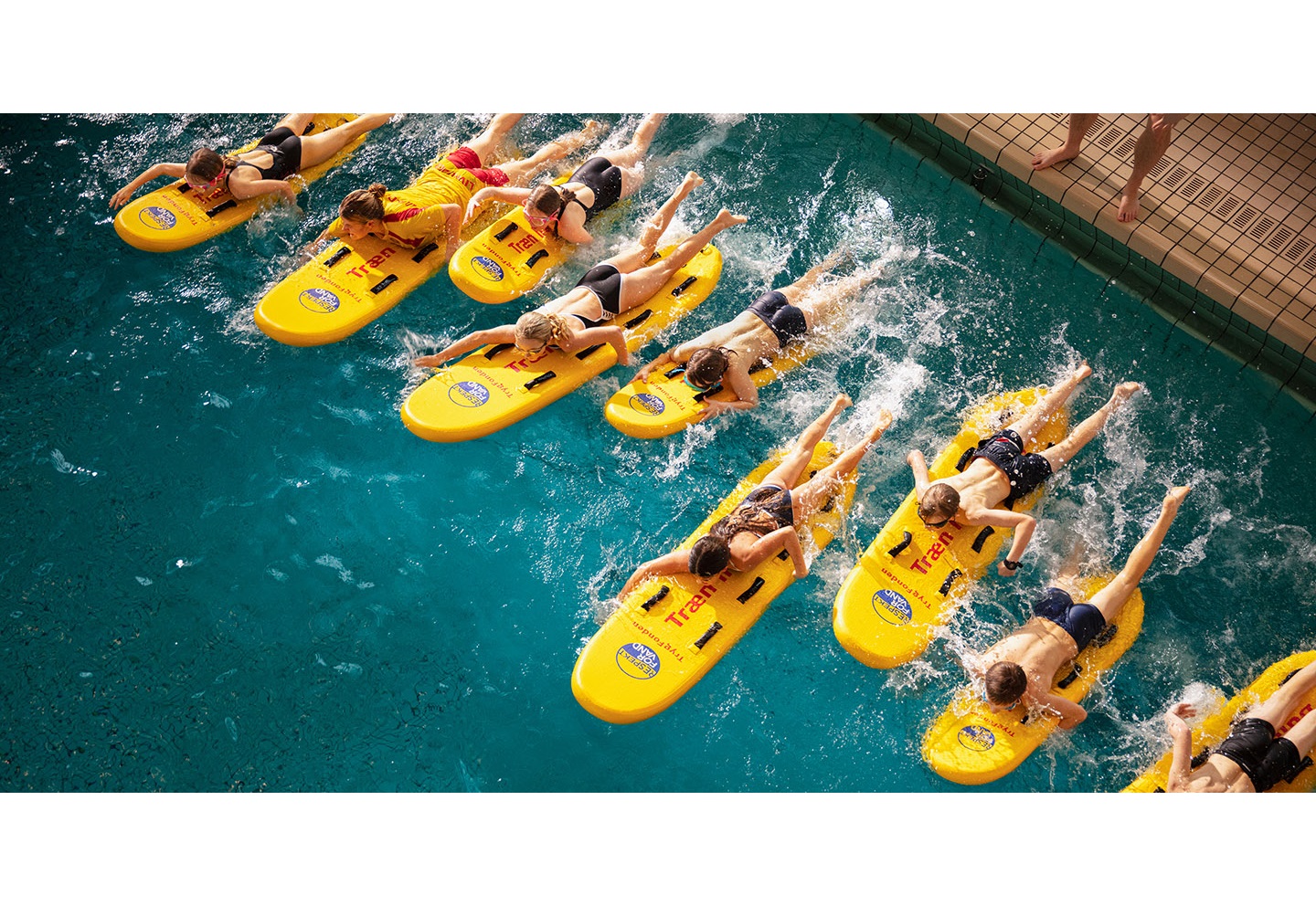 En gruppe børn på redningssurfbræt i svømmehallen